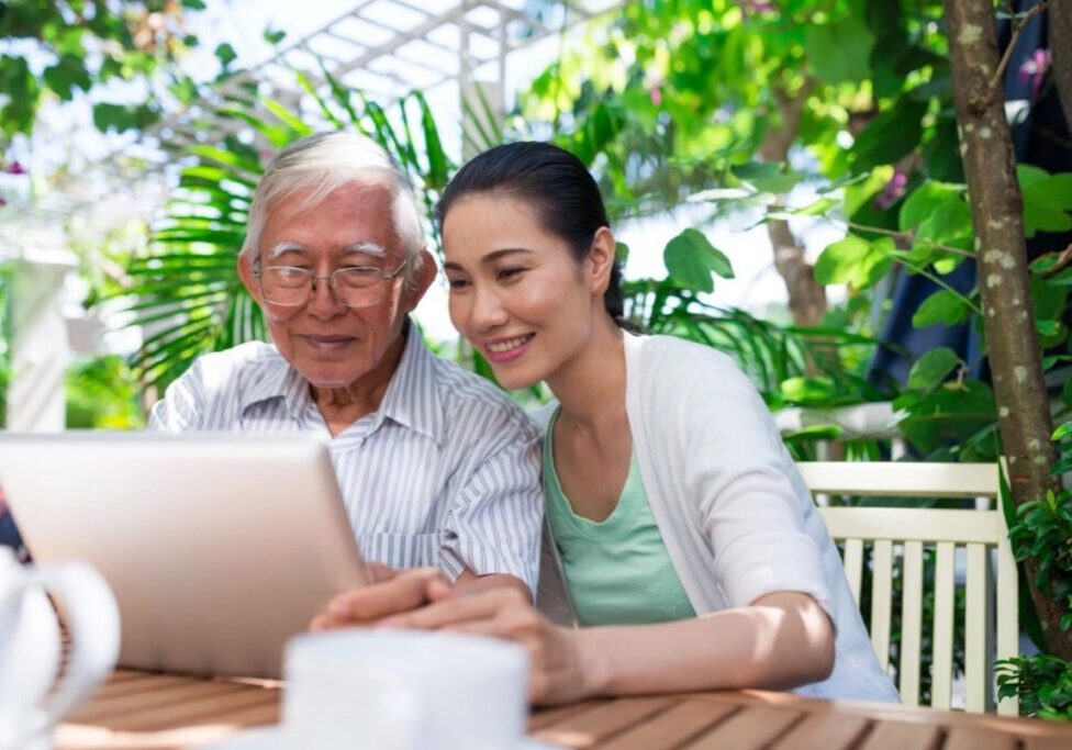A woman and an old man looking at a laptop.