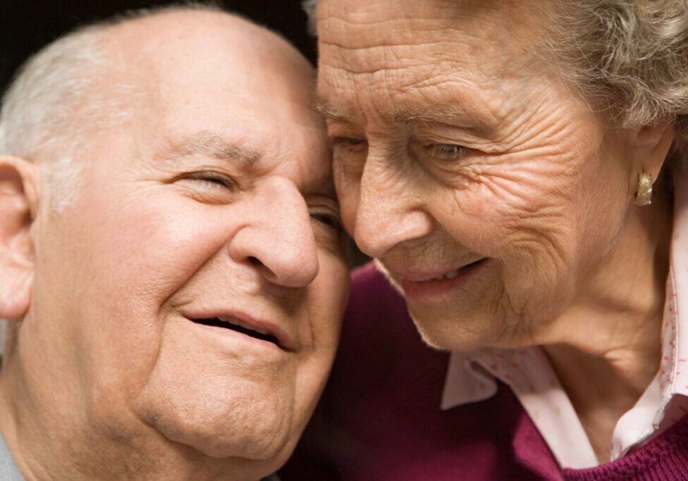 An older couple smiling at each other with their heads touching.